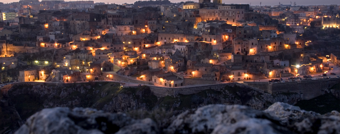 Historische Stadtansicht bei Dämmerung mit funkelnden Lichtern und markantem Turm.